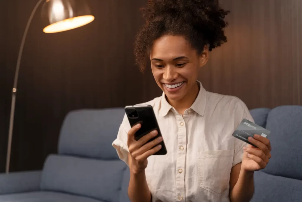 Mulher segurando um cartão de crédito e o celular, feliz após realizar uma compra com checkout simplificado