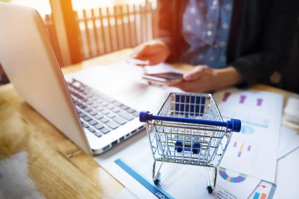 Carrinho de compras ao lado de notebook e gráficos, representando vendas no marketplace MadeiraMadeira.