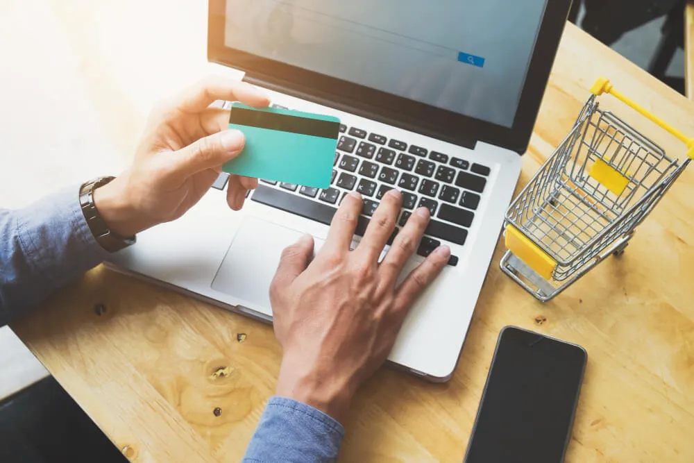pessoa mexendo no notebook com um cart&atilde;o na m&atilde;o representando compras vindas via amazon ads