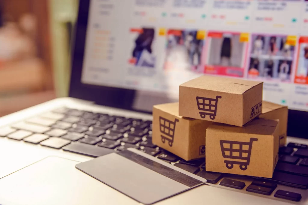 Pequenas caixas de papelão com ícone de carrinho de compras e um cartão de crédito sobre o teclado de um notebook aberto em uma loja virtual.
