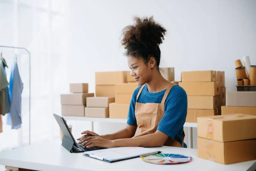 Vendedora trabalhando em loja online com caixas ao fundo e tablet, representando gestão de anúncios no Magalu Ads.