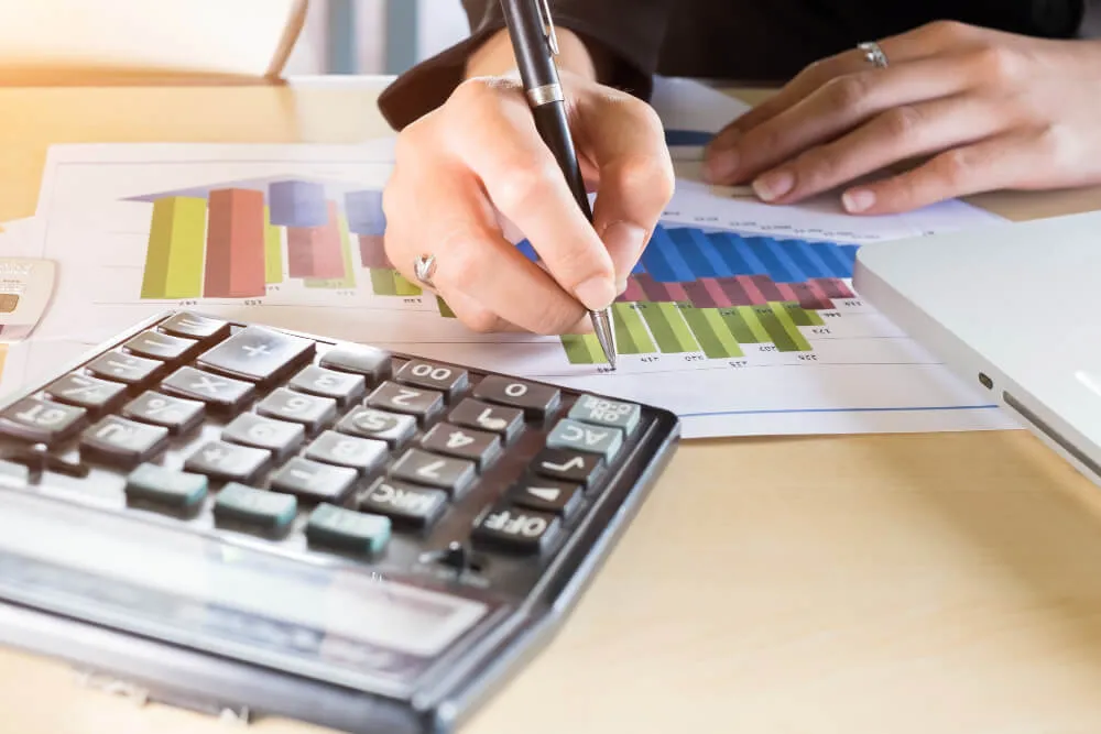 Mulher analisando gráficos com uma calculadora na mesa, checando os custos de migrar anúncio no Mercado Livre e shopee